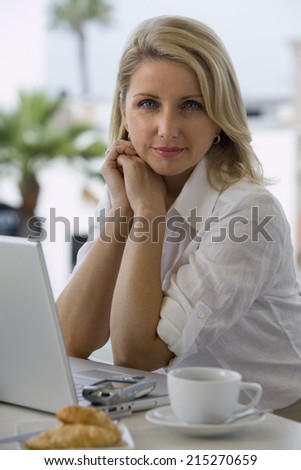 Businesswoman sitting at balcony table with laptop, smiling, side view, portrait