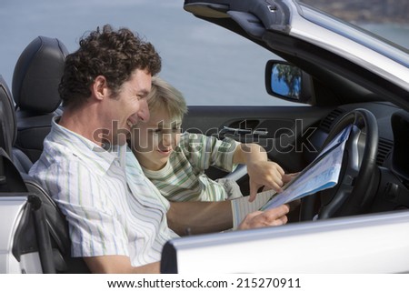 Father and son (6-8) sitting in convertible car, looking at road map, smiling, side view