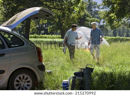 Senior man and adult son setting up camp in woodland clearing, tent in background, car in foreground