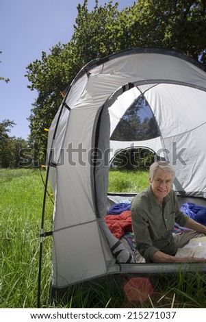 Senior man sitting inside tent in woodland clearing, looking at map, smiling, side view, portrait
