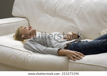 Man relaxing with feet up on sofa at home, listening to MP3 player, side view