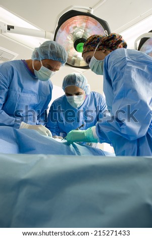 Surgeons in scrubs and surgical masks operating on patient, low angle view