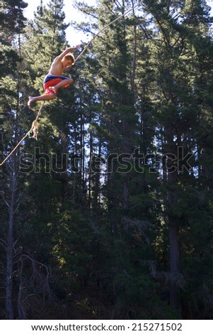 Teenage boy (12-14), in swimming shorts, swinging from rope above lake, side view, low angle view