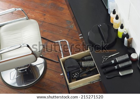 Barber\'s chair beside open draw of hair products, scissors and hairbrushes in salon, overhead view