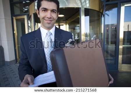 Businessman standing in front of revolving door, taking document from briefcase, smiling, portrait
