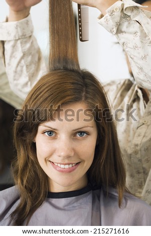 Hairdresser cutting woman\'s hair in salon, smiling, front view, close-up, portrait