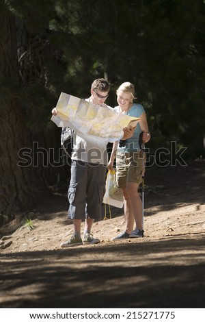 Couple hiking on woodland trail, consulting map, woman holding hiking pole, smiling