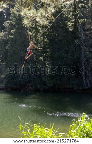 Boy , in swimming shorts, letting go of rope swing above lake