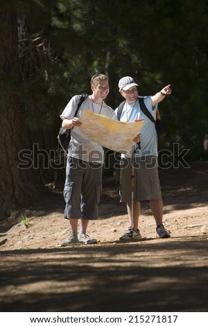 Senior man and adult son hiking on woodland trail, son consulting map, father pointing, smiling