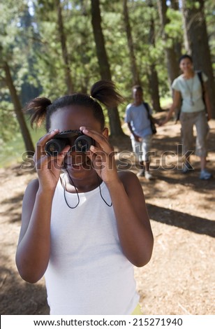 Family hiking on woodland trail, focus on girl looking through binoculars in foreground