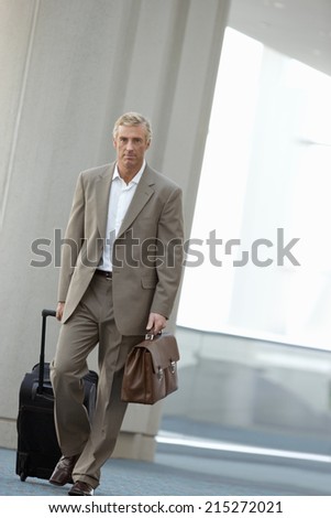 Businessman walking in airport with luggage (tilt)