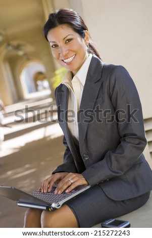 Businesswoman, in grey suit, using laptop in building arcade, smiling, side view, portrait (tilt)