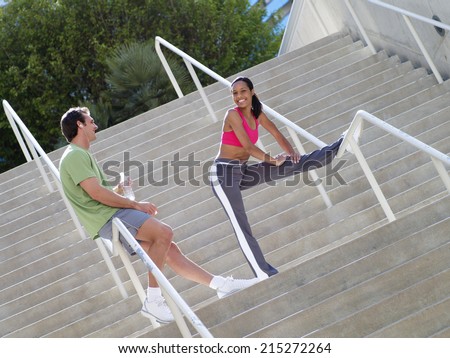 Couple, in sportswear, warming down from jog, man leaning against railing on steps, woman stretching leg (tilt)