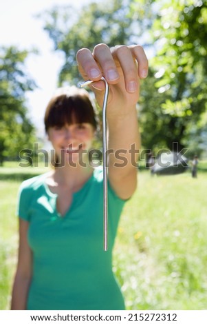 Woman standing woodland clearing, holding tent peg, smiling, close-up, front view, portrait