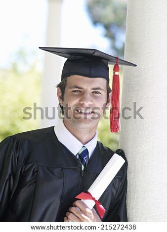 University student in graduation gown and mortar board holding diploma, smiling, close-up, portrait
