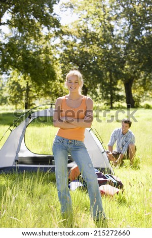 Young couple assembling dome tent on camping trip in woodland clearing, focus on woman, portrait