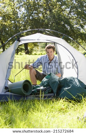 Young man assembling dome tent on camping trip in woodland clearing, smiling, portrait