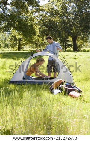 Young couple assembling dome tent on camping trip in woodland clearing, side view