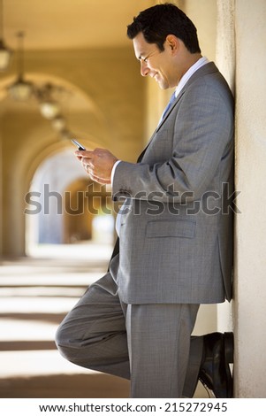 Businessman standing in building arcade, looking at text message on mobile phone, smiling, profile