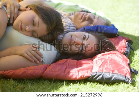 Family lying on sleeping bags in tent entrance on garden lawn, girl sleeping on motherÃ?Â¢Ã¢Â?Â¬Ã¢Â?Â¢s chest, woman smiling, side view, portrait