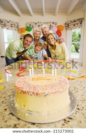 Three generation family celebrating birthday at home, smiling, portrait, birthday cake on table in foreground