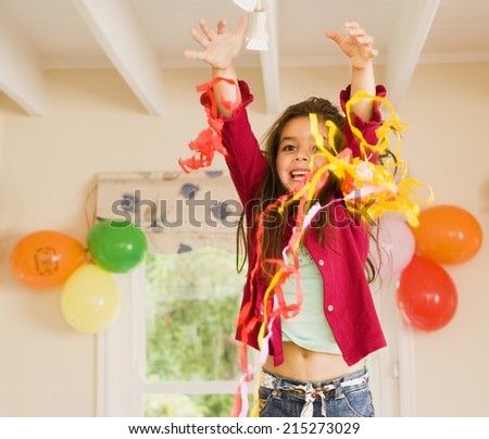 Excited girl (4-6) playing with streamers at birthday party, arms up, smiling, front view, portrait