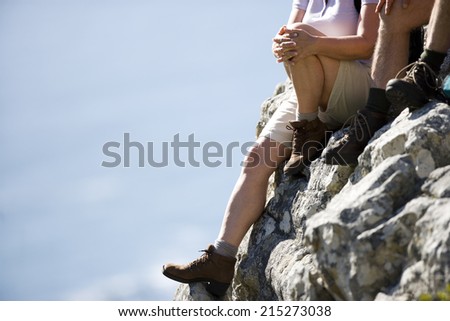 Mature couple, in hiking boots and shorts, sitting at edge of rock, looking at scenery, low-section