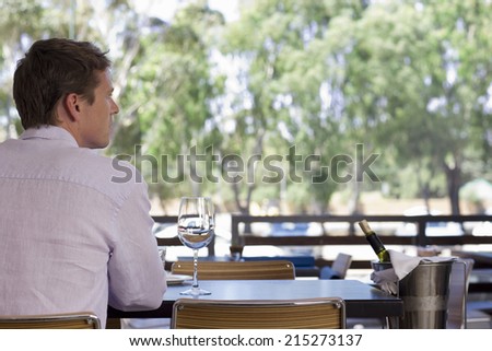 Man sitting at table on restaurant balcony with glass of wine and ice bucket, rear view