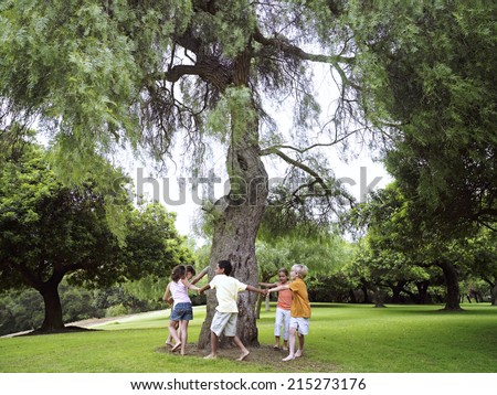 Group of children playing ring-a-ring-o\'roses in park, circling tree, holding hands