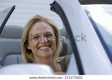 Woman sitting in driving seat of parked convertible car on driveway, smiling, close-up, portrait