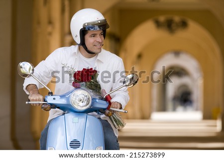 Man riding on motor scooter near colonnade, holding bouquet of red roses, smiling, front view