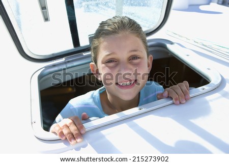 Girl (8-10) sticking head through open sailing boat cabin window, smiling, close-up, portrait
