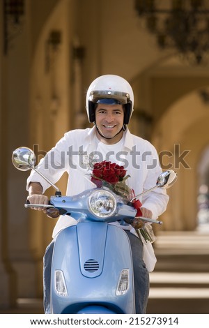 Man riding on motor scooter near colonnade, holding bouquet of red roses, smiling, front view, portrait