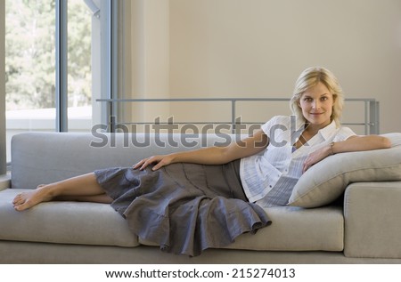 Woman relaxing with feet up on sofa at home, smiling, side view, portrait