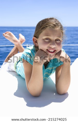 Girl (8-10) lying on front on deck of sailing boat out at sea, smiling, portrait