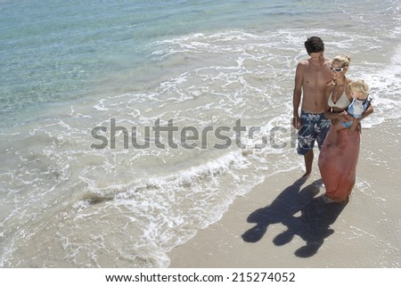 Family standing on beach in surf, woman carrying daughter (2-4), elevated view