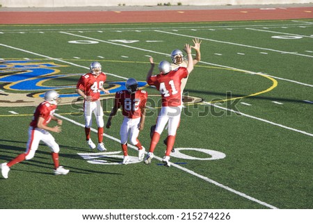 Opposing American football players competing for ball during competitive game, offensive receiver jumping up above rivals