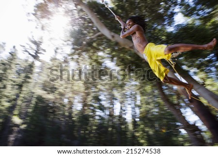 Boy (8-10), in yellow swimming shorts, swinging on rope above lake, low angle view (backlit)