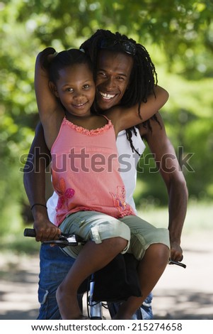 Father and daughter sitting on mountain bike, girl resting on handlebars, smiling, portrait
