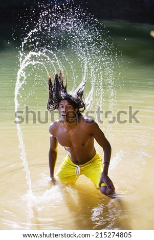 Man, in yellow swimming shorts, standing in shallow lake, tossing back long, wet dreadlocks