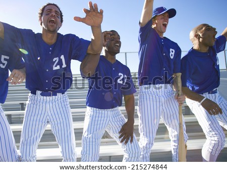 Excited baseball team jumping up from bench in stand during competitive baseball game, cheering, front view (backlit)