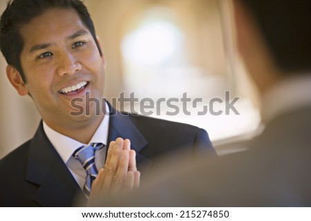 Respectful businessman greeting counterpart in building arcade, smiling (differential focus, tilt)