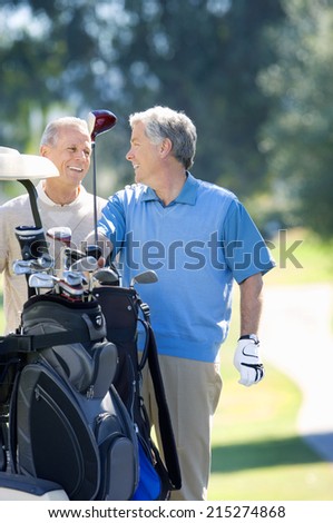 Two mature men playing golf, man in blue tank top taking driver from golf bag, smiling