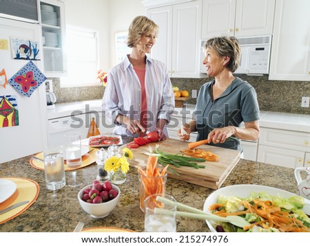 Senior woman and adult daughter cutting fresh vegetables on chopping board in kitchen, smiling