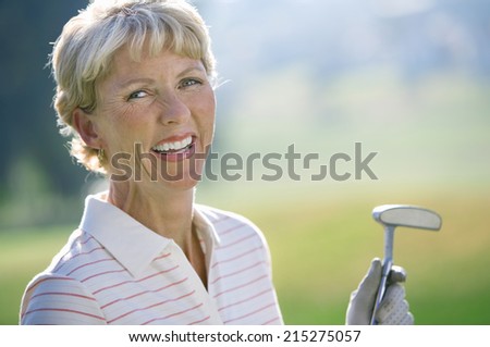 Mature woman in striped polo shirt and golf glove standing on golf course, holding putter, laughing, close-up, portrait