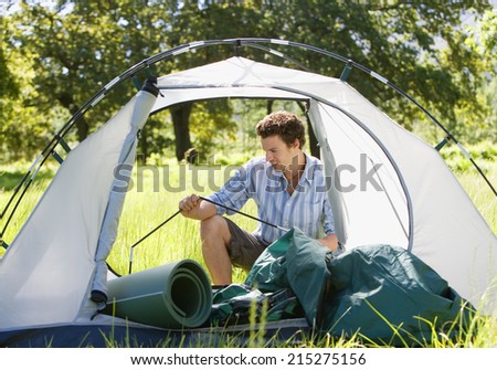 Young man assembling dome tent on camping trip in woodland clearing