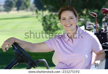 Mature woman, in pink polo shirt, sitting in golf buggy on golf course, smiling, side view, portrait