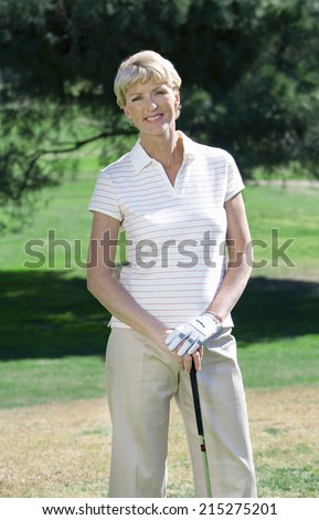 Mature woman, in striped short-sleeved shirt and golf glove, standing on golf course, leaning on golf club, smiling, front view, portrait