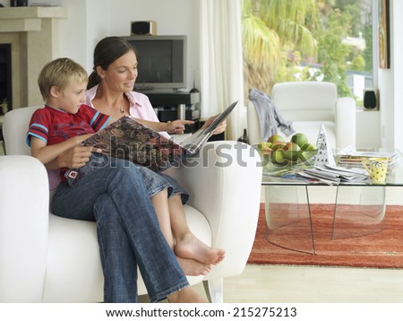 Mother and son (5-7) looking at photo album at home, boy in mother's lap in armchair, smiling