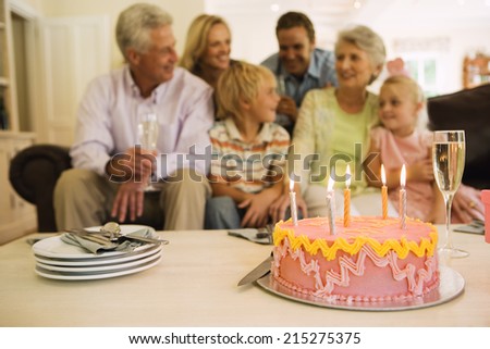 Three generation family sitting on sofa at home, birthday cake on coffee table in foreground